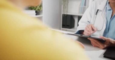 Beyaz üniformalı genç Asya 'lı kadın doktorun kapanışı harika haberler sunuyor. Sonuçları ya da belirtileri sağlık kliniğindeki masada oturan kız hastayla tartışıyor..