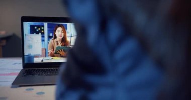 Dizüstü bilgisayar kullanan Asyalı iş kadını iş arkadaşlarıyla evdeki oturma odasındaki görüntülü görüşme planı hakkında konuşuyor. Gece aşırı yüklemeden, uzaktan, sosyal mesafeden, koronavirüs için karantinadan..