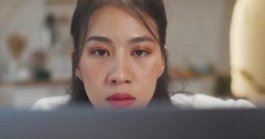 Genç Asyalı bayan serbest olarak dizüstü bilgisayardaki sunum işine ve mutfaktaki şirketle uzaktan görüşmenin finans projesine odaklanıyor. Kız öğrenci evde online öğreniyor. Yakın çekim..
