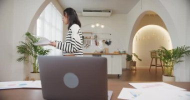 Dizüstü bilgisayar kullanan Asyalı iş kadını, mutfaktaki evde çalışırken iş arkadaşlarıyla görüntülü görüşme planı hakkında konuşuyor. İş yerinde uzaktan kontrol, sosyal uzaklık, koronavirüsü önlemek için karantina.