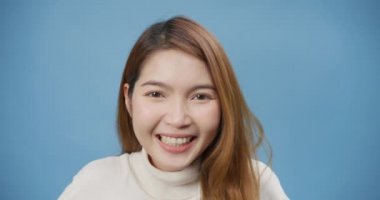 Yakın plan Asya 'lı genç bayan balıkçı yaka kazak giyer mavi arka plan üzerinde durur mutlu yüz, mükemmel beyaz dişler, eğlenceli, gülümseyen kahkahalar kameraya bakarak hayatın tadını çıkar. Pozitif kişilik duygusu.