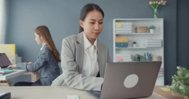 Genç Asyalı iş kadınları masadaki dizüstü bilgisayarlarını kullanarak iş yerindeki ofis masasında oturarak iletişim kuruyorlar. Uzak webinar, internet teknolojisi, yaşam tarzı sosyal uzaklık ve Coronavirüs 'ten sonra çalışma.