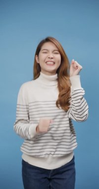 Yakın plan Asya 'lı genç bayan, mavi izole edilmiş arka plan üzerine oldukça neşeli bir süveter giyer, aşırı keyifli, neşeli, neşeli bir şekilde dans eder, gülümseyerek mutlu anların tadını çıkarırdı. Ayakta dans eden, el kaldıran. Dikey ekran.