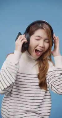 Genç Asya 'lı bayan telefonda süveter giyer mavi arka planda izole edilmiş favori müzik listesindeki yeni popüler şarkıları dinler. Gençler, müzik, duygu konsepti. Dikey ekran.