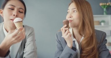 Bir grup Asyalı yaratıcı takım çalışanı iş yerindeki çalışma masasında oturup gülerek dondurma yerken eğleniyor. Ortak işbirliği, iş arkadaşı takım çalışması.
