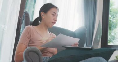 Dizüstü bilgisayar kullanan Asyalı iş kadını, oturma odasından çalışırken iş arkadaşlarıyla görüntülü görüşme planı hakkında konuşuyor. İş yerinde uzaktan, sosyal uzaklık, korona virüsünün önlenmesi için karantina.