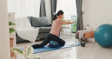 Spor kıyafetleri içinde genç ve çekici Asya 'lı güçlü bir kadın. Oturma odasında spor topuyla ısınıyor. Ev karantina idmanı ve spor..