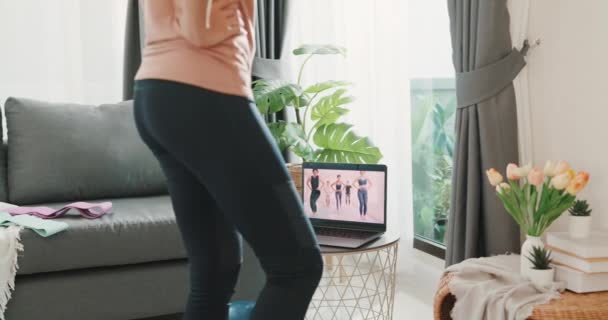 年轻迷人的亚洲女人 穿着运动服站在地板上的垫子上 和一群人一起参加了一个针对家里客厅初学者的关于笔记本电脑练习瑜伽的视频会议 — 图库视频影像
