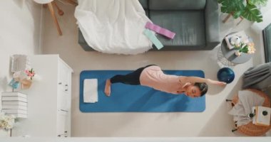 Spor kıyafetleri içinde genç ve sportif Asya 'lı güçlü bir kadının oturma odasında yeni başlayanlar için ısınma egzersizi yogası yapması. Ev karantina idmanı ve spor..