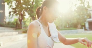 Genç Asyalı atlet bayan, akşamları şehir parkında egzersiz yaparken boynuna havlu yapıştırarak yüz ve boyuna ter siliyor. Spor ve spor dışında sağlıklı yaşam tarzı konsepti.
