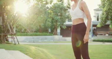 Beautiful young Asia athlete lady exercises doing squat jumps after running on urban stairs at park environment in evening sunset. Outside workout and fitness healthy lifestyle concept.