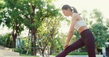 Güzel, genç Asyalı atlet bayan, akşam günbatımında şehir parkında koştuktan sonra vücudunu ısıtarak egzersiz yapıyor. Spor ve spor dışında sağlıklı yaşam tarzı konsepti.