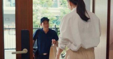 Young Asian delivery man in blue navy uniform knock door home delivery grocery online shopping to woman customer in front of the door and woman accept paper bag at house. Delivery service concept.