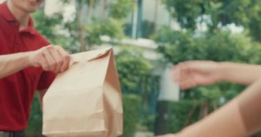 Close-up Young happy Asian delivery man with bicycle in red uniform carry case box knock door home shopping online food paper bag to woman in front of door at house. express food delivery concept.