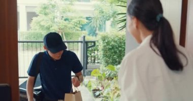 Young Asian delivery man in blue navy uniform knock door home delivery grocery online shopping to woman customer in front of the door and woman accept paper bag at house. Delivery service concept.