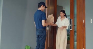 Young Asian delivery man in blue navy uniform knock door home delivery grocery online shopping to woman customer in front of the door and woman accept paper bag at house. Delivery service concept.