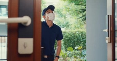Young Asian delivery man wear mask in blue navy uniform carry case box knock door home online shopping paper bag to woman in front of door lady scan QR code payment on smartphone at house concept.