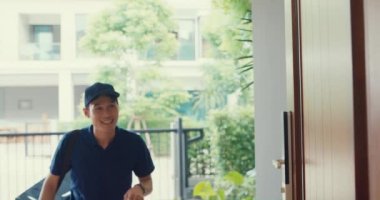 Young Asian delivery man in blue navy uniform knock door home delivery grocery online shopping to woman customer in front of the door and woman accept paper bag at house. Delivery service concept.
