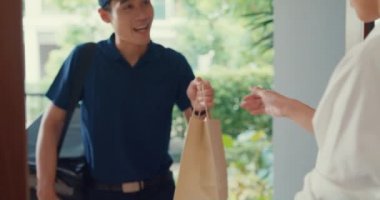 Close-up Young Asian delivery man in blue navy uniform carry case box knock door home online shopping to woman in front of the door and lady sign accept paper bag on smartphone at house concept.