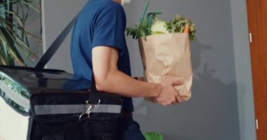 Close-up Young Asian delivery man in blue navy uniform carry case box knock door home deliver grocery online shopping to customer front of door at house. Express delivery concept.