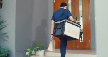 Young Asian delivery man wear mask in blue navy uniform carry case box knock door home delivery online shopping paper bag to customer front of door at house. Express food delivery concept.