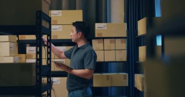 Asian businessman use barcode scanner scan paper box in shelf and put data in digital tablet cut stock online data information detail for express delivery at warehouse. Startup small business concept.