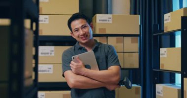 Successful Asian businessman stand front of shelf hold on digital tablet and barcode scanner smiling and looking at camera proud of business in warehouse at night. Startup small business concept.