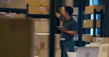 Asian businessman use barcode scanner scan paper box in shelf and put data in digital tablet cut stock online data information detail for express delivery at warehouse. Startup small business concept.