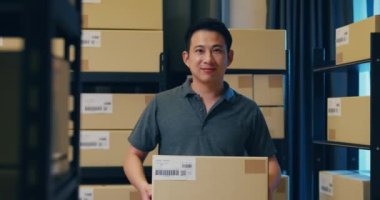 Successful Asian businessman stand front of shelf hold cardboard paper box smiling and looking at camera proud to present of his business in warehouse at night. Startup small business concept.