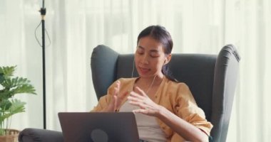 Young asia female girl or university student sit on sofa chair with computer laptop wear earphone listen music chill and singing take a rest work in living room at house. Home lifestyle concept.