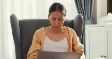 Young asia female girl or university student sit on sofa chair with computer laptop feel pain, hurt shoulder from hard work overtime in living room at home. Office syndrome, Work life balance concept.