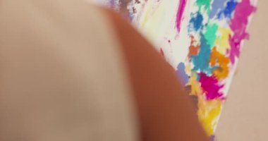 Asian toddler girl with apron sit sofa chair front of painting canvas put acrylic color on palette use palette knife blend color and do abstract art in living room at home. Lifestyle kid concept.