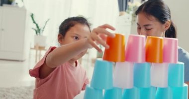 Close-up Asian toddler little girl with mom sit on carpet with happy moment playing colorful stacks cup toy in living room at home. Family spend fun time together, Creative lifestyle for kid concept.