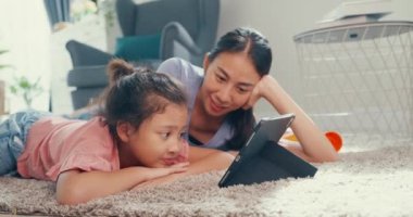 Asian toddler little girl daughter with mother watch digital tablet on carpet floor having fun, joyful moment in living room at home. Family spend time together, Creative lifestyle for kid concept.