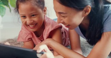 Close-up Asia toddler little girl daughter with mother play on digital tablet on carpet floor having fun, joyful in living room at home. Family spend time together, Creative lifestyle for kid concept.