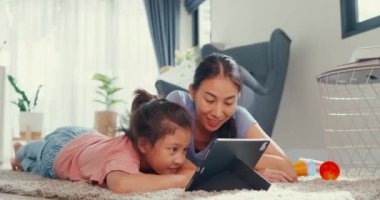 Asian toddler little girl daughter with mother watch digital tablet on carpet floor having fun, joyful moment in living room at home. Family spend time together, Creative lifestyle for kid concept.