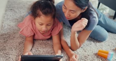 Close-up Asia toddler little girl daughter with mother play on digital tablet on carpet floor having fun, joyful in living room at home. Family spend time together, Creative lifestyle for kid concept.