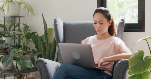 年轻的亚洲女人坐在机翼椅上 头脑清醒 用笔记本电脑思考在客厅温室里种满植物的想法 Coronavirus Stay Home Work Home Concept — 图库视频影像