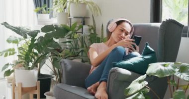 Sıradan kulaklık takan genç Asyalı kadın kanat koltuğunda oturuyor. Akıllı telefon kullanıyor. Rahat müzik dinliyor, evde dinleniyor. Kapalı alandaki bitkilerle sıcak bir ev, şehir ormanı kavramı.