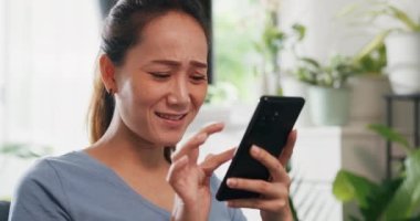 Yakın plan, genç Asyalı kadın rahat bir site giyer. Akıllı telefon kullanır. Oturma odasındaki ev bitkilerinde internetten alışveriş yapmak heyecan verici. Heyecanlı ve şaşırmış bir kadın elinde cep telefonu tutuyor..