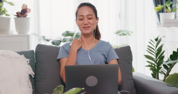 Ung Asiatisk Kvinne Med Uformell Øretelefon Sittende Sofaen Bærbar Videosamtale – stockvideo