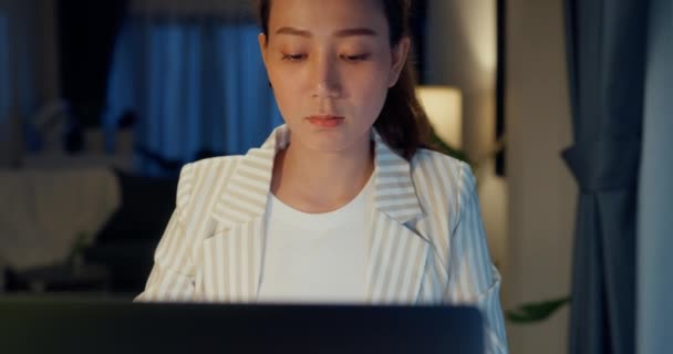 若いアジアのビジネスマンの女性は 自宅の夜に居心地の良いリビングルームの屋内工場でのスクリーンチェックレポート会議にラップトップコンピュータと紅茶のカップで机の正式な座面を着用します 残業の概念 — ストック動画