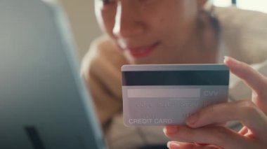 Mutlu, gülümseyen, beyaz krem pijamalı bir Asyalı kız üniversitesi. Kabarık, rahat bir yatağa uzan. Kredi kartı kullan..