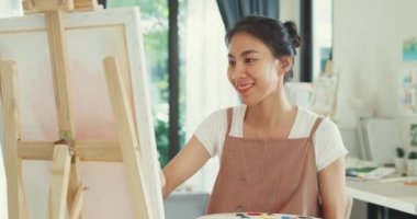 Mutlu genç Asya kadınları palet renginde önlük giyer tuvale fırça boyası sürer evdeki rahat atölyede sanat çalışması yapar. Çağdaş Ressam Soyut Modern Sanat, Yaratıcılık ve İnsan Konsepti.