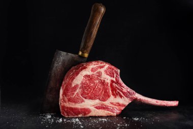Fresh meat tomahawk steak with knife on old wooden board. Dark background. 