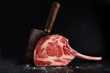 Fresh meat tomahawk steak on old wooden board. Dark background. Closeup