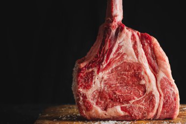 Fresh meat tomahawk steak on old wooden board. Dark background. Closeup