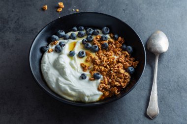 Appetizing homemade muesli with berries and yogurt served in bowl on dark background. 