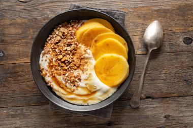 Tasty appetizing autumnal bowl with yogurt oat and persimmon on wooden table. 
