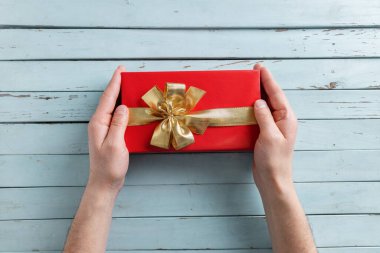 Man holding giftbox with golden ribbon in hands on blue vintage table